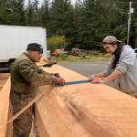 Master Carver Wayne Price, left, works on the canoe in the Angoon High School parking lot. (Photo by Jonathan Wunrow)