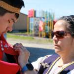 Jeannette Kookesh helps her nephew, Triston Rose-Shaquanie, with his regalia. Angoon students named and launched a dugout canoe on June 19. (Photo by Claire Stremple/Alaska Beacon)