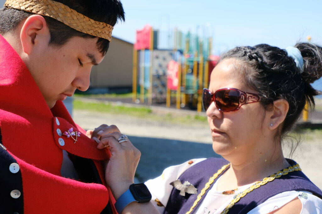 Jeannette Kookesh helps her nephew, Triston Rose-Shaquanie, with his regalia. Angoon students named and launched a dugout canoe on June 19. (Photo by Claire Stremple/Alaska Beacon)