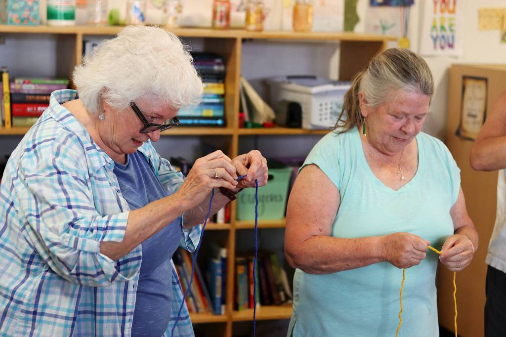 Judy Cavanaugh (left) and Mary Miller learn how to separate yarn into strands without using scissors during a Weaving Our Pride project workshop Friday at the Zach Gordon Youth Center. (Mark Sabbatini / Juneau Empire)