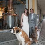 Maura Selenak and Brandon Howard celebrate their marriage in front of the Amalga Distillery they have created together in the historic 1937 AELP building. They stand  with their dogs Walter and Wallaby  on their wedding day in 2017 on the corner of Second and Seward Streets with the custom-built pot still, made in Kentucky, visible through the large front window. (Photo by Ben Huff, courtesy of Maura Selenak)