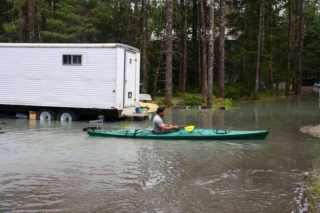 A man paddles a kayak through a flooded driveway toward a house along View Drive on Saturday evening. (Mark Sabbatini / Juneau Empire)