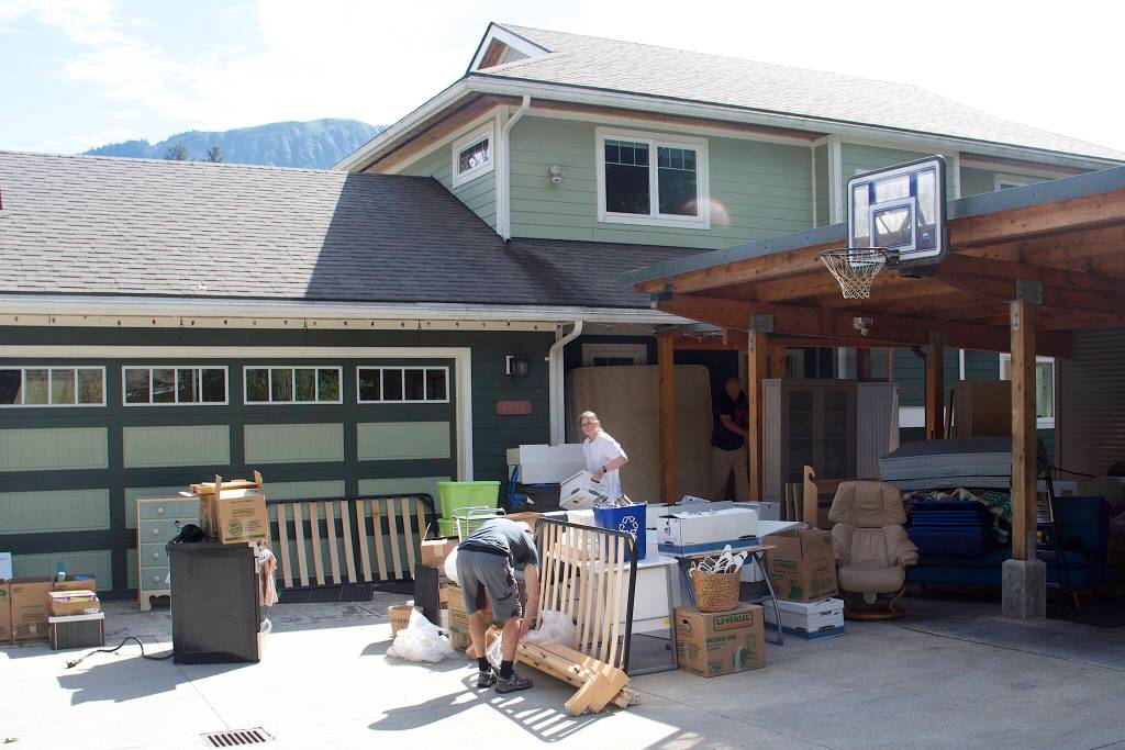 Local residents move belongings out of a home along the Mendenhall River that has about one-fourth of the structure hanging over the bank at midday Sunday, following massive erosion caused by record flooding Saturday. (Mark Sabbatini / Juneau Empire)