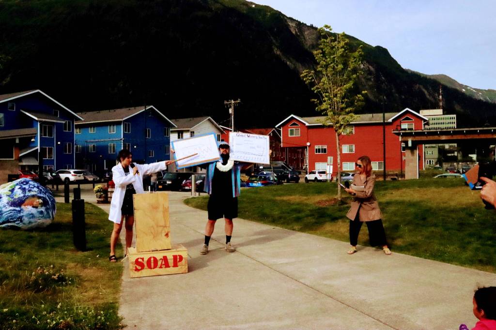 Natalia Spengler points to data on signs held up by Conor Lendrum as Ellie Pisel-Davis describes the significance of the data during the annual Climate Fair for a Cooler Planet on Saturday at Overstreet Park. (Meredith Jordan / Juneau Empire)