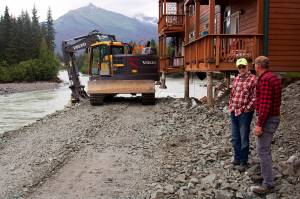 Steve Bradford (left) and Mark Kissel, both vice presidents of the Riverside Condominiums Homeowners Association, discuss repairs to two of the complexs buildings on Wednesday as a bulldozer places rock fill under a corner of one building exposed by erosion during record flooding of the Mendenhall River last Saturday. (Mark Sabbatini / Juneau Empire)