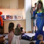 A collection of books such as And Tango Makes Three, which are the targets of bans in many states, await on a shelf at the Mendenhall Public Library during a Drag Storytime on Saturday as performer Lituya Hart Monroe (right) enters the room and greets children. (Mark Sabbatini / Juneau Empire)