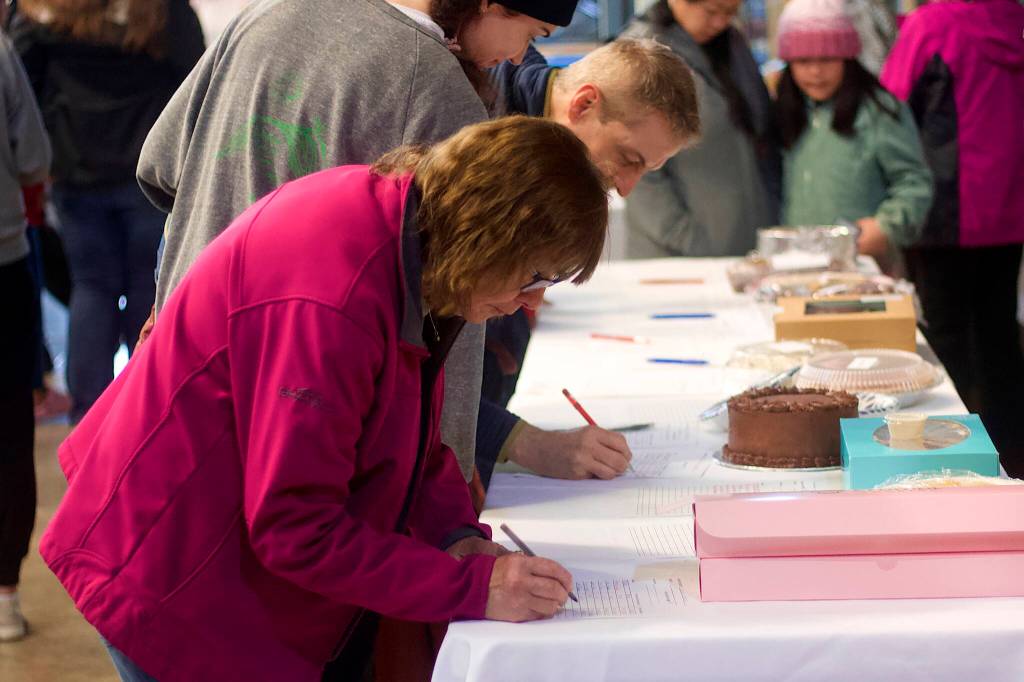 Diane Diekmann joins bidders in a silent dessert auction as part of a fundraiser Saturday night at Thunder Mountain High School on behalf of people affected by record flooding of the Mendenhall River earlier this month. Diekmann also made four of the more than 100 desserts sold at the auction. (Mark Sabbatini / Juneau Empire)