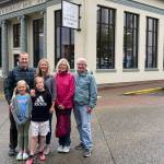 Three generations of the Behrends-Gruening family stand outside the bank founded by B.M. Behrends. Standing from left: Jack Vines, Caroline Gruening Vines, Anne Gruening (great-granddaughter of B.M. Behrends), and Win Gruening (grandson of Governor and Senator Ernest Gruening). Young Norah and Jack Vines stand in front. (Photo by Laurie Craig)