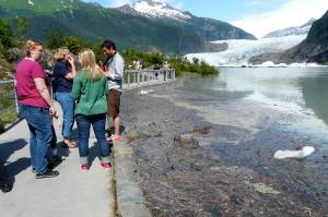 A crowd gathers on the Photo Point Trail footbridge near Mendenhall Glacier Visitor Center to witness flooded Mendenhall Lake during the first jökulhlaup on July 20, 2011. Sloshing debris beside the bridge floats atop the flooding lake. The lake reached 10.92 feet that year. (Photo by Laurie Craig)