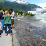A crowd gathers on the Photo Point Trail footbridge near Mendenhall Glacier Visitor Center to witness flooded Mendenhall Lake during the first jökulhlaup on July 20, 2011. Sloshing debris beside the bridge floats atop the flooding lake. The lake reached 10.92 feet that year. (Photo by Laurie Craig)