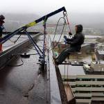 Brick Engstrom (right) connects his harness to a rope on a crane-like device Thursday morning that allows him, co-worker Colton Baucom and two other people to rappel down the 11-story State Office Building as they clean it with pressure washers. The first such cleaning in at least a decade, which began a week ago, is expected to take about another month. (Mark Sabbatini / Juneau Empire)