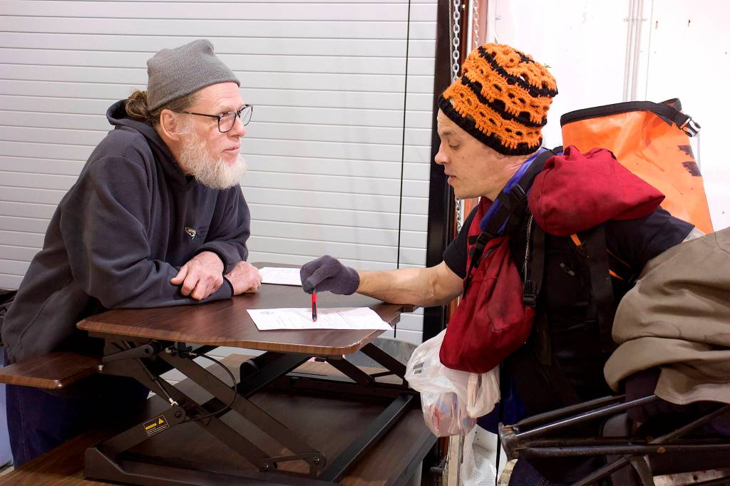 Vernon Ollenberger, left, a staff member at the citys new cold weather emergency shelter, goes over the rules on a sign-in form with Garrett Derr. Both men spent the summer at Mill Campground until it closed a week ago Monday. (Mark Sabbatini / Juneau Empire)