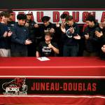 Teammates and friends applaud after Juneau-Douglas High School: Yadaa.at Kalé senior Lamar Blatnick signs a letter of intent Wednesday in the JDHS gymnasium to play baseball for Dallas Christian College. (Klas Stolpe for the Juneau Empire)