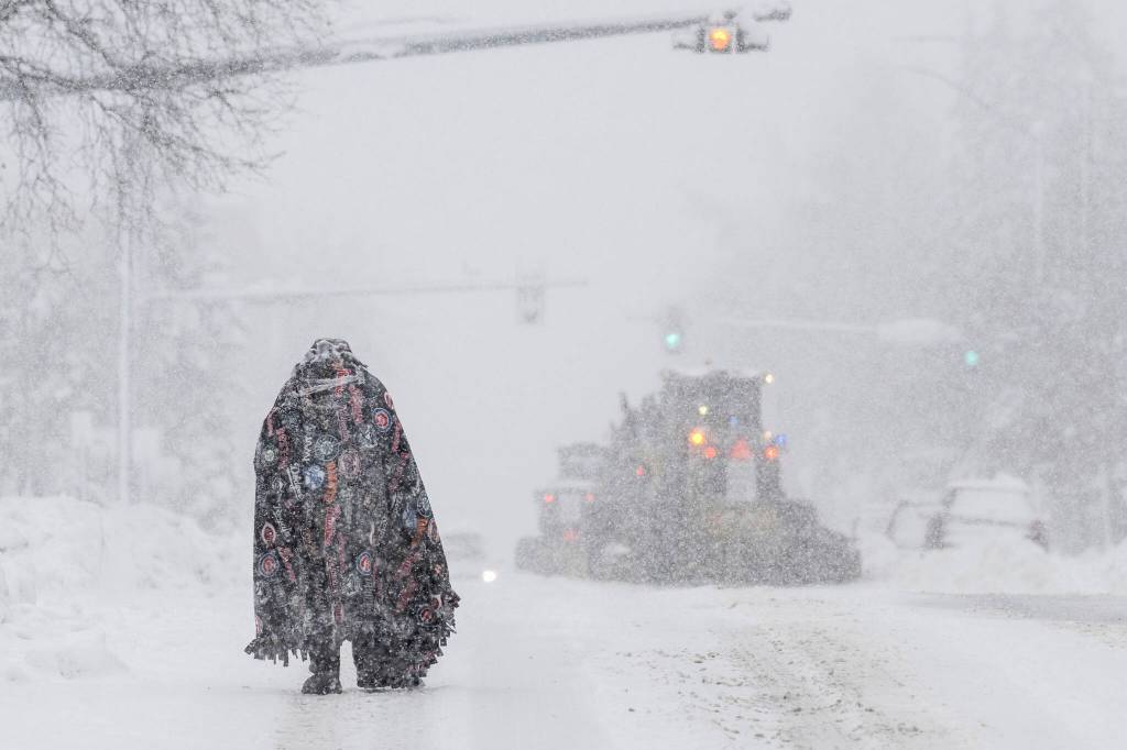 A pedestrian takes cover under a blanket on Cordova Street as plows clear the roadway on Thursday in Anchorage. Four homeless people have died in Anchorage in the last week, underscoring the citys ongoing struggle to house a large houseless population at the same time winter weather has returned, with more than 2 feet (0.61 meters) of snow falling within 48 hours. (Marc Lester/Anchorage Daily News via AP)