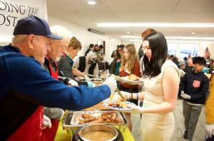 Former Juneau Volunteer Fire Department Chief Jim Carroll (left), and Juneau Mayor and Alaska Attorney General Bruce Botelho serve traditional Thanksgiving dinner dishes to Marzena Whitmore, a volunteer who serves the filled plates to diners during the communal meal hosted by The Salvation Army Juneau Corps at the Juneau Yacht Club on Thursday. (Mark Sabbatini / Juneau Empire)
