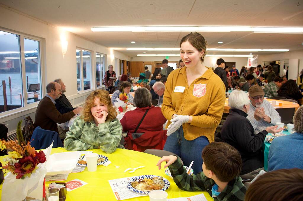 Keeley Riley, a volunteer at the communal Thanksgiving dinner hosted by The Salvation Army Juneau Corps, offers takeout containers to a family of diners at the Juneau Yacht Club on Thursday. (Mark Sabbatini / Juneau Empire)