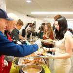 Former Juneau Volunteer Fire Department Chief Jim Carroll (left), and Juneau Mayor and Alaska Attorney General Bruce Botelho serve traditional Thanksgiving dinner dishes to Marzena Whitmore, a volunteer who serves the filled plates to diners during the communal meal hosted by The Salvation Army Juneau Corps at the Juneau Yacht Club on Thursday. (Mark Sabbatini / Juneau Empire)