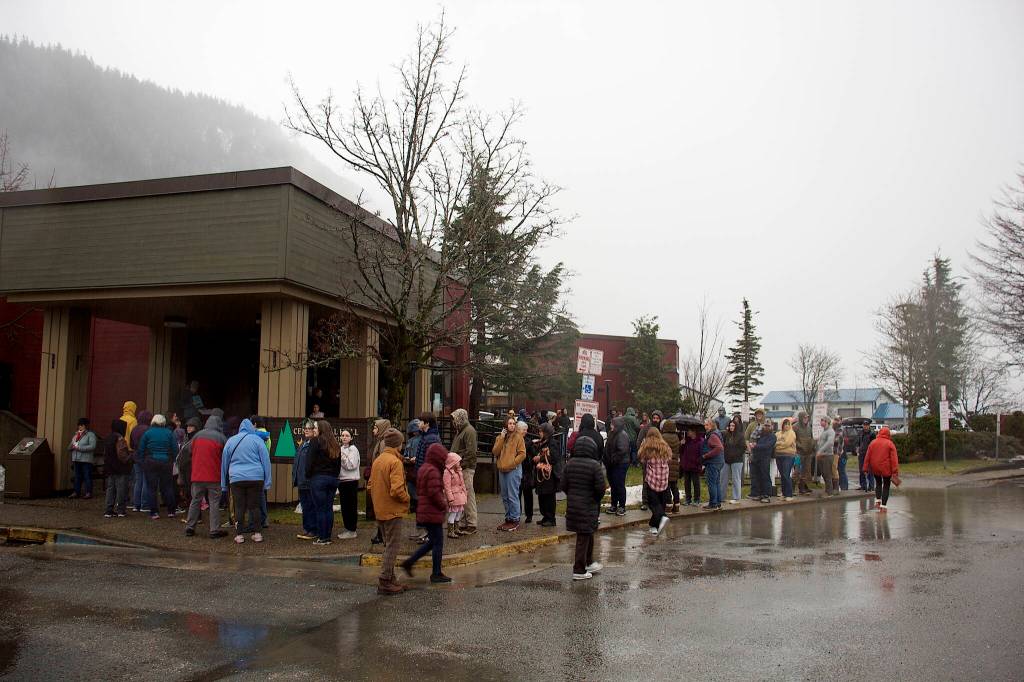 A few dozen people wait in the rain outside Centennial Hall for the start of the Juneau Public Market just before noon on Friday. (Mark Sabbatini / Juneau Empire)