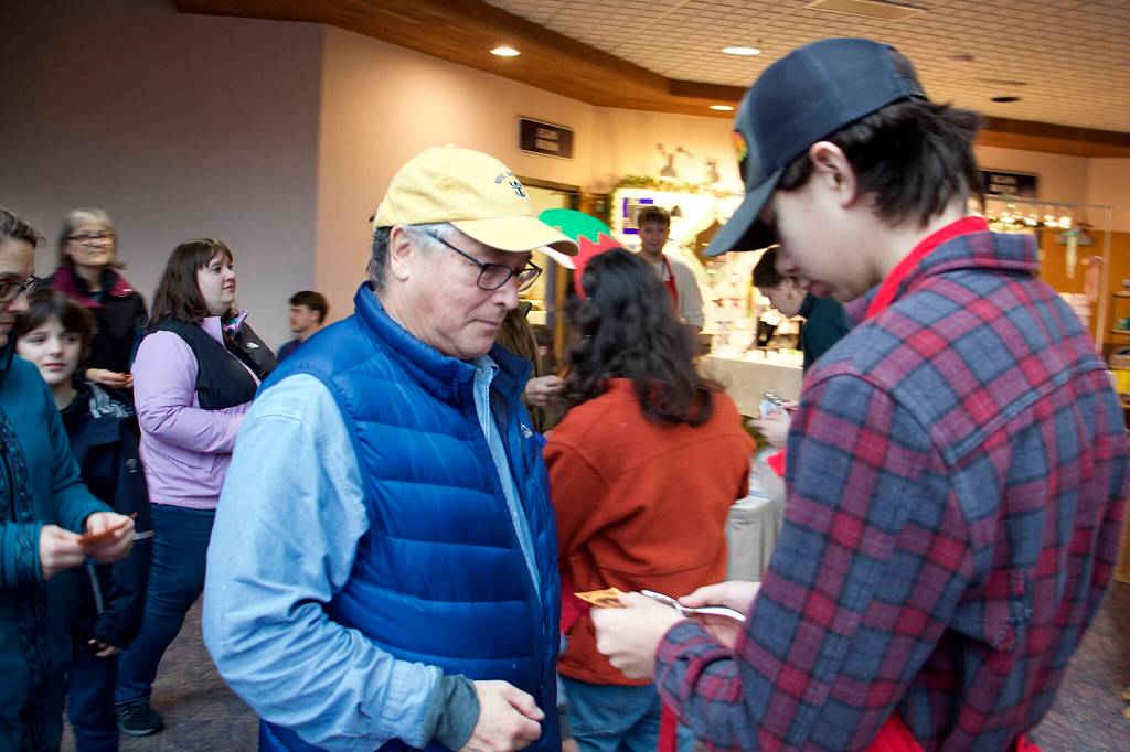 Larry Gamez (left) has his admission ticket to the Juneau Public Market punched on Friday. He was the second in line to enter the market at Centennial Hall, arriving an hour early. (Mark Sabbatini / Juneau Empire)