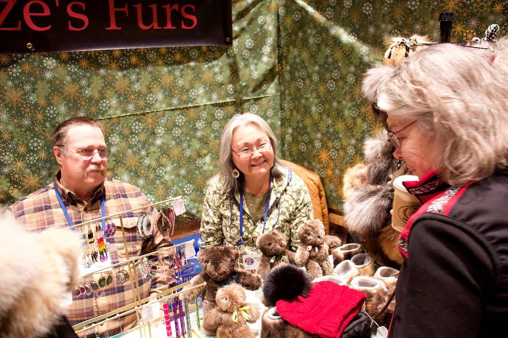 Todd and Annie Fritze (left) talk to Cheryl Benson about fur products sold at the couples booth at the Juneau Public Market on Friday at Centennial Hall. The couple travels from Dillingham each year to spend Thanksgiving with family in Juneau sell items made from furs they trap. (Mark Sabbatini / Juneau Empire)