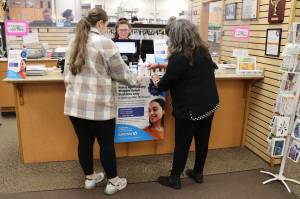 Cheyenne Latu (left), a pharmacy technician at Rons Apothecary Shoppe, and business co-owner Gretchen Watts hang a poster at the front counter Thursday announcing the stores closure after Dec. 6 as Jessica Kirtley, another pharmacy technician, works at the front register. The nearby Safeway supermarket has agreed to take the prescriptions of all customers as well as hire all of the independent pharmacys employees, according to the co-owners who are retiring. (Mark Sabbatini / Juneau Empire)