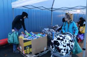 Michael Carter selects chips from a large box while Kalie Purkey wheels their 1-year-old daughter, Oaklynn Carter, along the row of tables at the Southeast Alaska Food Banks weekly food pantry on Thursday. (Mark Sabbatini / Juneau Empire)