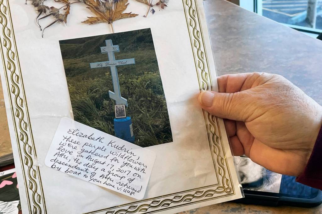 George Kudrin holds a photo of his wifes grave, Dec. 1, 2023, in Anchorage, Alaska, with flowers gathered on Attu Island pressed inside the laminate cover. His wife was the second to last living descendant of Attu, Alaska, whose entire population was captured by the Japanese during World War II and sent to Japan until being liberated after the war. She died in February 2023, and her brother Gregory Golodoff, the last living Attu resident, died nine months after she did. (AP Photo/Mark Thiessen)