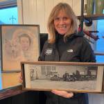 Wings Airways co-owner Holly Johnson displays a photo of the Johnson familys 1920s Ford dealership on the site of todays Merchants Wharf. Behind her is a painting of Juneau dog mushing celebrity Mary Joyce who owned Taku Lodge in the 1930s. Wings Airways partners with current lodge owners Ken and Michelle Ward who provide wild salmon meals for flightseeing guests in summer. (Photo Laurie Craig)
