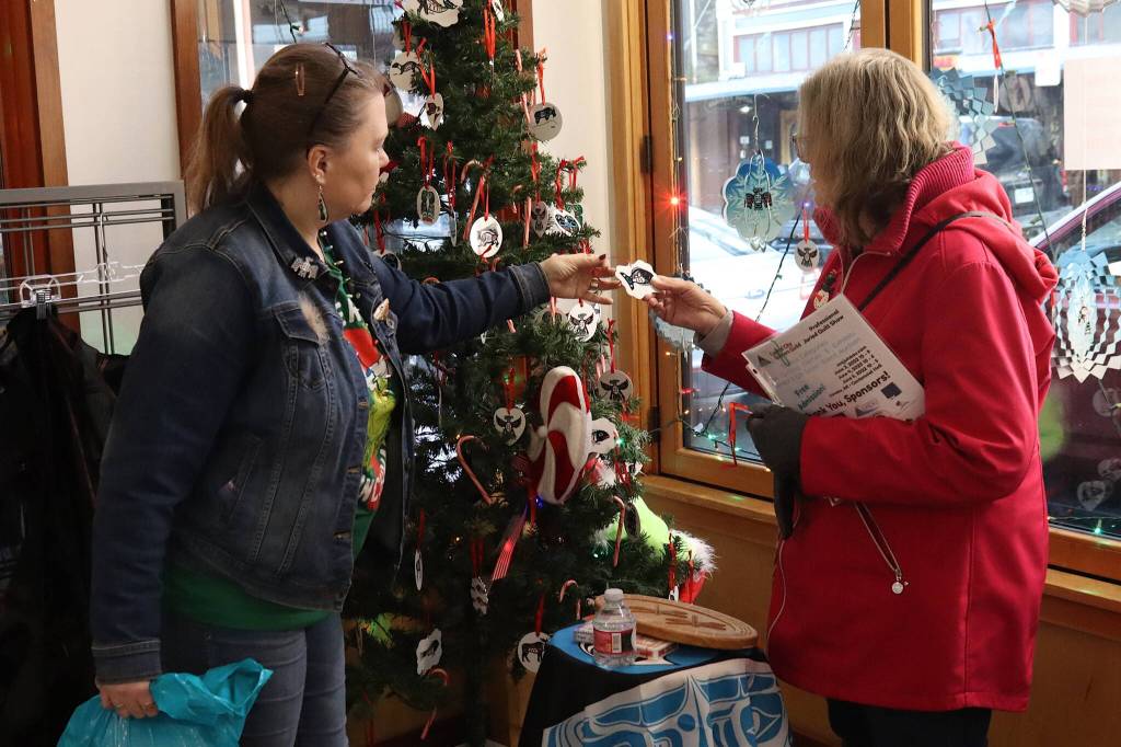 Misty Chilton (left), wife of Tlingit artist Doug Chilton, shows a Christmas ornament to Raydene Garrison at Indigenous Art Doug Chilton Designs on Monday. The downtown shop is closing on Dec. 24 as its namesake owner is planning to operate by mail order from Washington State. (Mark Sabbatini / Juneau Empire)