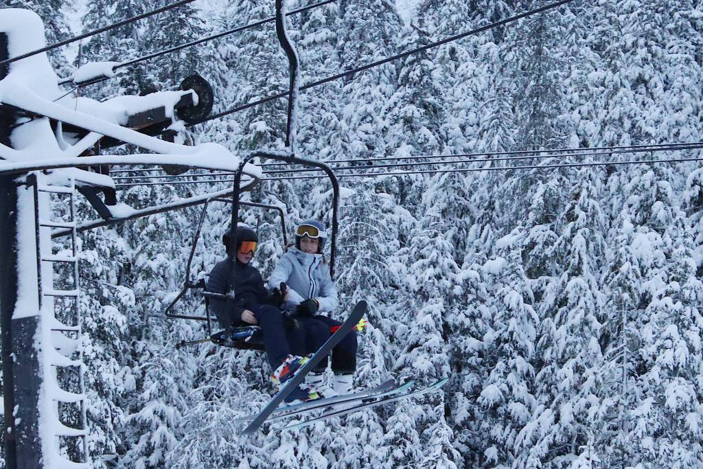 Two skiers settle into a lift chair as they pass trees with fresh snow Wednesday morning at Eaglecrest Ski Area. (Mark Sabbatini / Juneau Empire)
