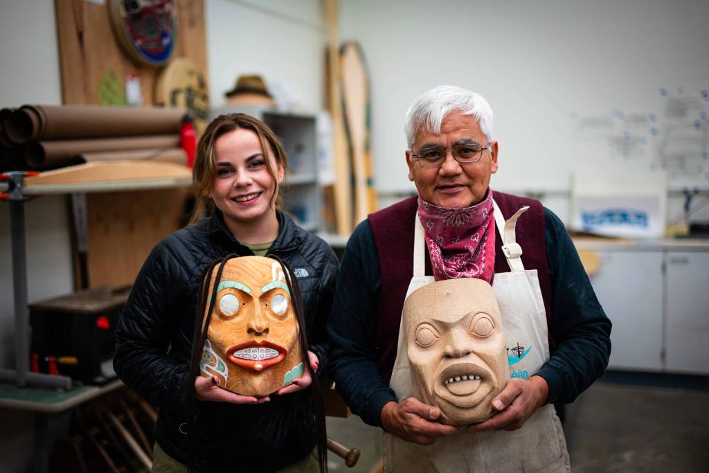 Master Lingít Carver Wayne Price and former University of Alaska student Andrea Cook hold masks done in Prices university class. Price works to protect the standtalls, the massive red cedar trees that are needed to carve totem poles, canoes and other cultural art pieces he sees as integral to a strong future in the arts. (Photo by Bethany Goodrich)