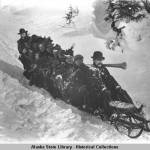 Ten adults pack onto a long sled to slide down a snow-packed slope. Often city streets were used for this winter activity. One man holds a horn, ready to warn pedestrians of the oncoming sledders. (Alaska State Library  Historical Collections P87-1258)