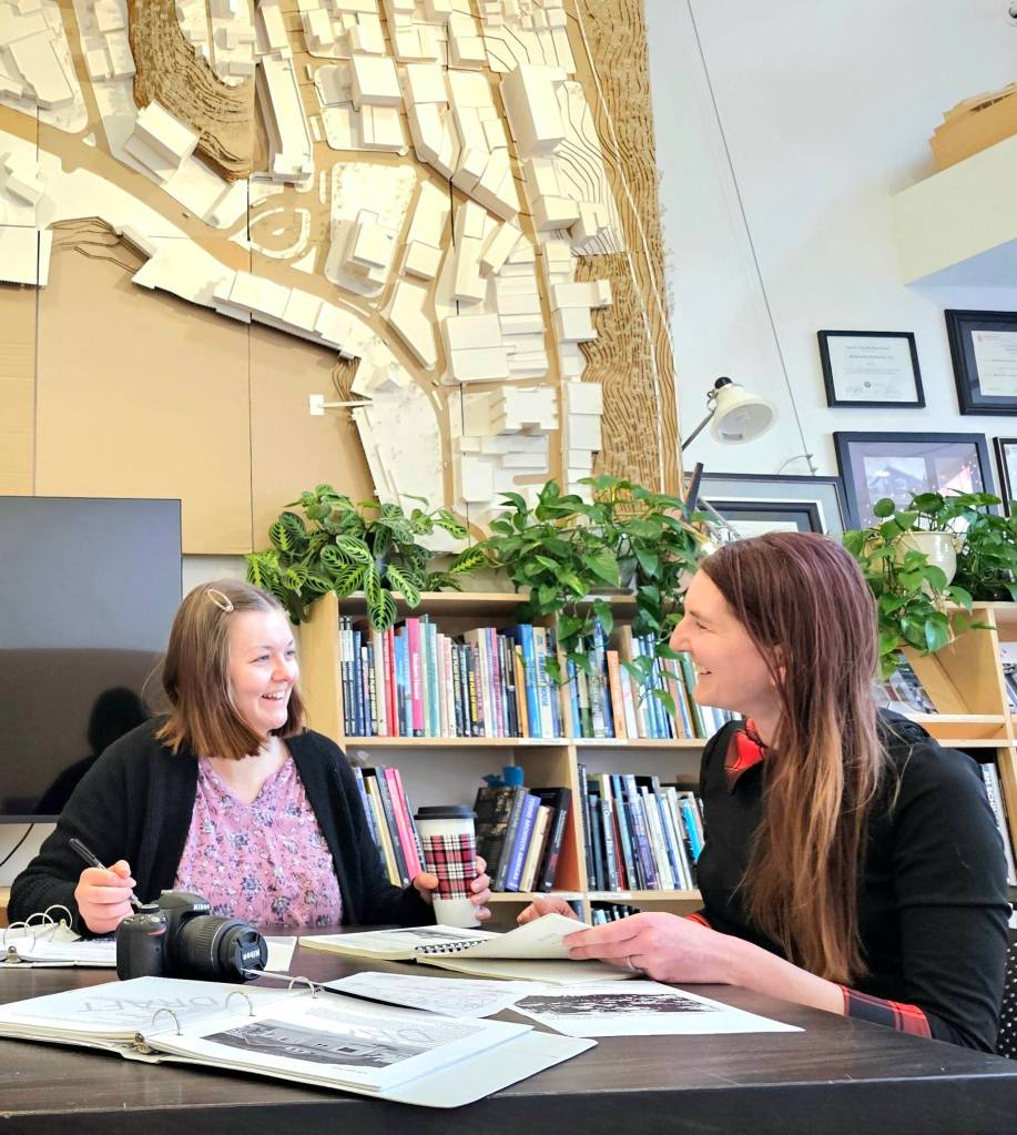 Architectural intern Summer Putman and historical architect Shannon Crossley discuss the townsite survey they prepared. On the wall behind them is a 9-foot by 12-foot three-dimensional model of downtown Juneau created by colleagues at NorthWind Architects. (Photo by Rose Evans)