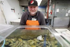 Mauka Grunenberg looks at live oysters for sale on Aug. 29, 2022, at Sagaya City Market in Anchorage. The oysters came from a farm in Juneau. Oysters, blue mussels and sugar, bull and ribbon kelp are the main products of an Alaska mariculture industry that has expanded greatly in recent years. (Photo by Yereth Rosen/Alaska Beacon)