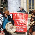 Pat White, center, holds a large banner on the steps of the Alaska State Capitol during a climate rally on Thursday. She also participated in a rally at the Capitol earlier this week calling for a ceasefire in Gaza. (Mark Sabbatini / Juneau Empire)