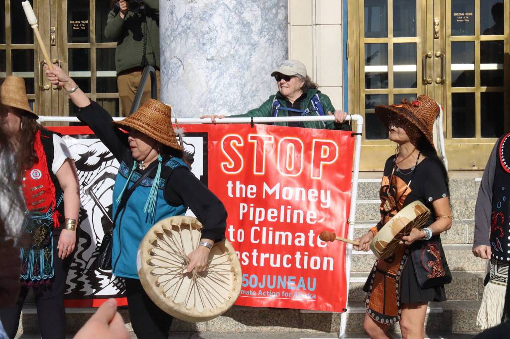 Pat White, center, holds a large banner on the steps of the Alaska State Capitol during a climate rally on Thursday. She also participated in a rally at the Capitol earlier this week calling for a ceasefire in Gaza. (Mark Sabbatini / Juneau Empire)