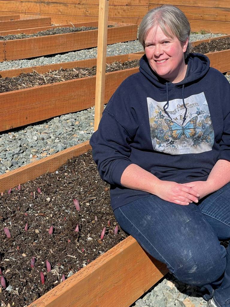 Bobbi Epperly sits beside one of her flower beds at Pederson Hill Farm. (Laurie Craig / For the Juneau Empire)