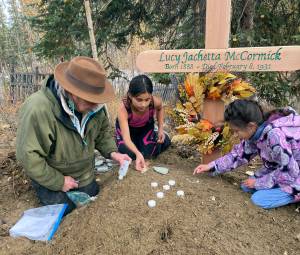 In this Sept. 29, 2023, photo at the grave of Lucky Pitka McCormick, her granddaughter Kathleen Carlo, left, and McCormicks great-great-grandchildren Lucia, center, and Addison Carlo place candles and stones on the grave during a reburial ceremony in Rampart, Alaska. Pitka was one of the Lost Alaskans sent to a mental hospital in the 1930s. Her grave was recently discovered, and family members brought her back to Alaska for a proper burial. (Wally Carlo via AP).
