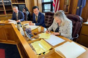 Rep. DeLena Johnson, R-Palmer and co-chair of the House Finance Committee, signs the committees version of the state operating budget on Friday. Looking on is Rep. Neal Foster, D-Nome, and at background is Rep. Frank Tomaszewski, R-Fairbanks. (James Brooks/Alaska Beacon)