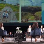 The Newtok Mothers assembled as a panel at the Arctic Encounter Symposium on April 11 discuss the progress and challenges as village residents move from the eroding and thawing old site to a new village site called Mertarvik. Photographs showing deteriorating conditions in Newtok are displayed on a screen as the women speak at the event, held at Anchorages Denaina Civic and Convention Center. (Yereth Rosen/Alaska Beacon)