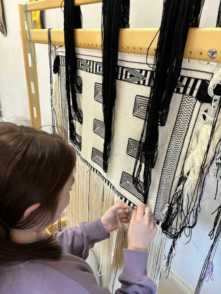 Kinsie Young weaves on her child-size robe for the Youth Pride Robe project. (Photo courtesy of Lily Hope)