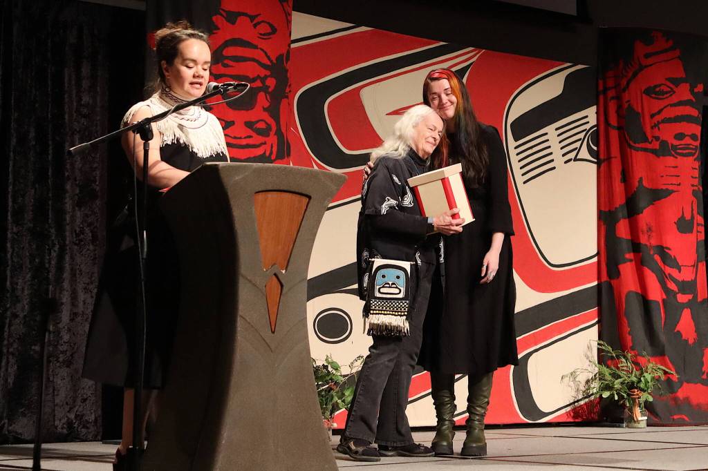 Lily Hope (left) offers a presentation of gratitude to longtime weaving teacher Kay Field Parker, who hugs Rae Mills after receiving a gift during a ceremony organized by Hope featuring Ravenstail regalia at Centennial Hall on Tuesday night. (Mark Sabbatini / Juneau Empire)