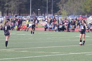 Finley Sullivan (right), a senior forward who broke her finger in practice a month ago, performs a kickoff to Ruby Rivas (#9), a senior midfielder who tore an anterior cruciate ligament in January, during the final home game of the season for the Juneau-Douglas High School: Yadaa.at Kalé girls soccer team Saturday at Adair-Kennedy Field. Both players came out of the game moments later during an intentional stoppage in play. (Mark Sabbatini / Juneau Empire)