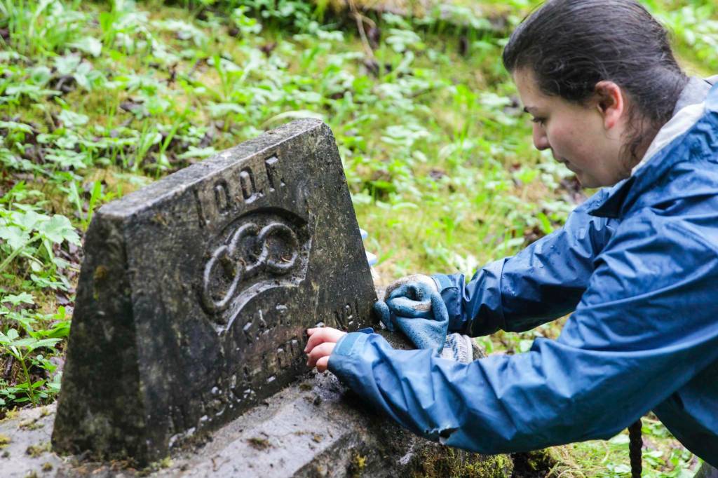 Adriana Botelho works to clean a headstone as part of restoring the Lawson Creek Cemetery on May 22, 2021. (Michael S. Lockett / Juneau Empire file photo)