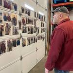 Jim Geraghty looks at the many photos posted on his shop wall of smiling owners of new/used jackets. (Laurie Craig / Juneau Empire)