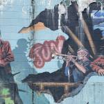 Artist Arnie Weimer includes two locals portraits wearing the original dark red halibut jackets in the mural he painted on a concrete exterior wall near Second and Franklin Streets. (Laurie Craig / Juneau Empire)