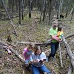 Leanne Bulger kneels at a hole in the forest floor that pumps out cool air. At her shoulder is her daughter Rose. Rosie Fordham, Bulgers co-worker, holds Bulgers daughter Violet. (Photo by Ned Rozell)