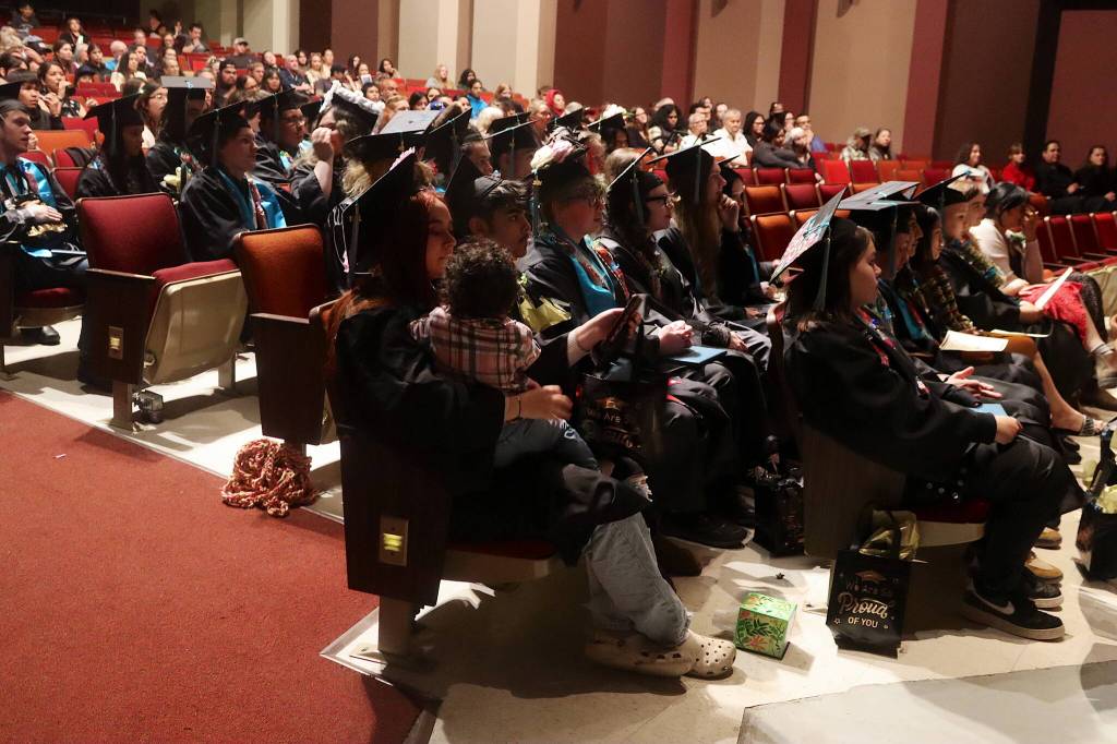 Graduating seniors at Yaaḵoosgé Daakahídi High School listen to departing words from Principal John Paul during Sundays commencement ceremony in the Juneau-Douglas High School: Yadaa.at Kalé auditorium. (Mark Sabbatini / Juneau Empire)