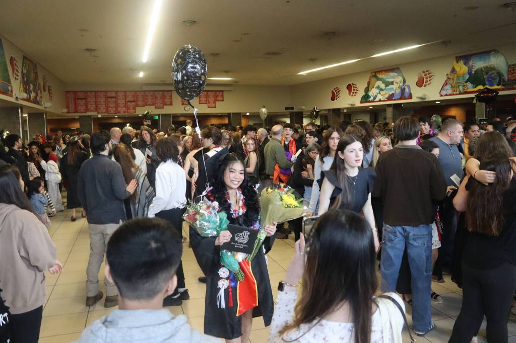 Arielle Gemino, 18, shows off her new diploma and gifts as family members take photos in the commons area at Juneau-Douglas High School: Yadaa.at Kalé following Sundays commencement ceremony. (Mark Sabbatini / Juneau Empire)