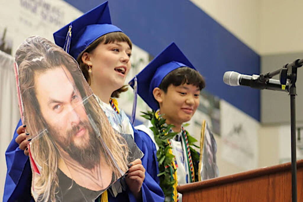 Jade Hicks and Mackenzie Lam jokingly hold up cardboard cutouts of Aquaman actor Jason Momoa, saying they took them from the classrooms of teachers who have a celebrity crush on him, during a joint speech at Thunder Mountain High Schools commencement ceremony on Sunday. (Jasz Garrett / Juneau Empire)